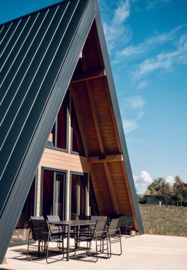 Cabin Haus Holzhaus mit spitzem Dach, großen Fenstern und Terrasse, umgeben von grünem Rasen.